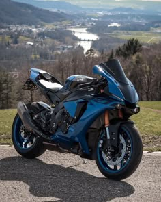 a blue motorcycle parked on the side of a road next to a lush green hillside