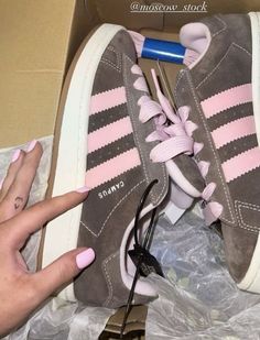 a woman's pink and grey adidas sneaker in a box with her hand on the laces