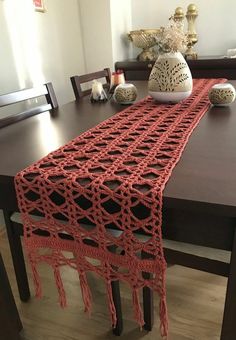 a table with a red crocheted runner on top of it next to a vase