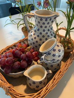 a basket with grapes, milk and other items sitting on a table next to potted plants