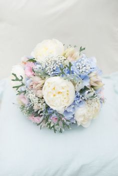 a bridal bouquet with white and blue flowers on a light blue pillow in front of a white background