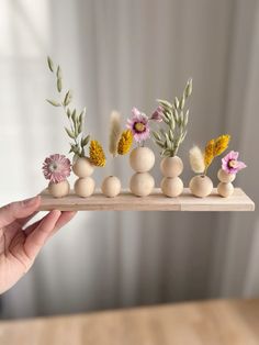 a person holding a wooden tray with flowers and rocks on it in front of a window