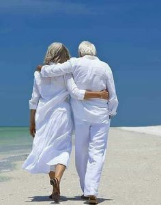 an older couple walking on the beach with their arms around each other's back