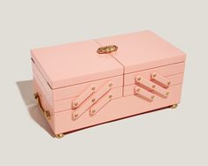 a pink jewelry box with gold handles and rivets on the top, sitting on a gray surface