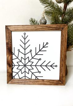 a wooden frame with a black and white snowflake drawn on the side in front of a pine tree