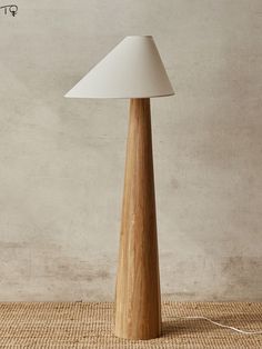 a wooden table lamp with a white shade on the top and bottom, in front of a beige wall