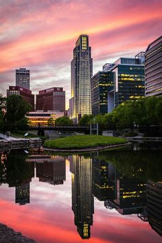 the city skyline is reflected in the water at sunset, with pink and purple clouds