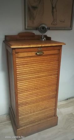 an old fashioned wooden cabinet with shutters on the doors and drawers, in front of a painting