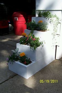 three white planters with flowers in them on the sidewalk