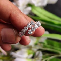 a person holding a ring in their hand with flowers in the backgrouf