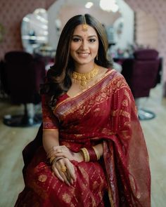 a woman in a red and gold sari sitting on a chair smiling at the camera