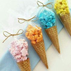 four ice cream cones filled with colorful flowers on top of a blue cloth covered table