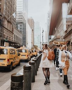 two women walking down the street in front of taxi cabs and people on sidewalk