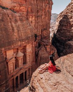 a woman in a red dress sitting on top of a rock formation next to a cliff