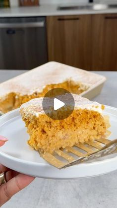 a person holding a plate with a piece of cake on it and a fork in the foreground