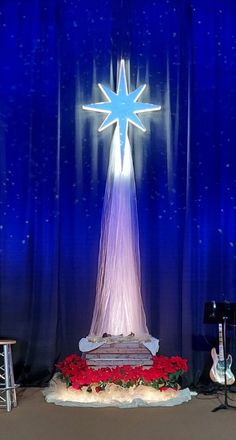 a lighted christmas star on display in front of a stage backdrop with red flowers and guitars