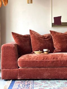 a red couch with two pillows on it in front of a rug and a painting