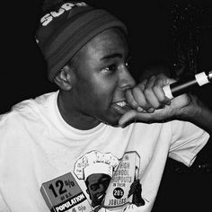 a black and white photo of a young man holding a microphone to his mouth while wearing a t - shirt