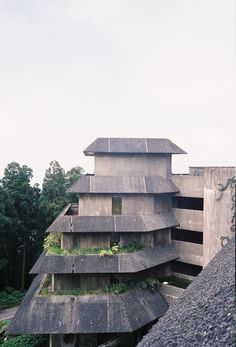 an unusual building with plants growing out of it's roof and side walls, in front of trees