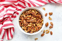 a white bowl filled with nuts on top of a red and white striped towel next to a spoon