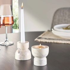 two marble candle holders sitting on top of a table next to a glass of wine