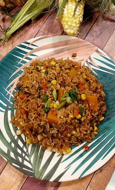 a plate full of rice and vegetables on a wooden table with corn in the background