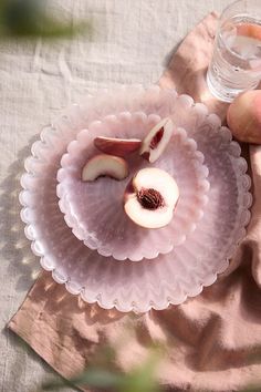 two pieces of fruit on a pink plate next to a glass of water and peaches