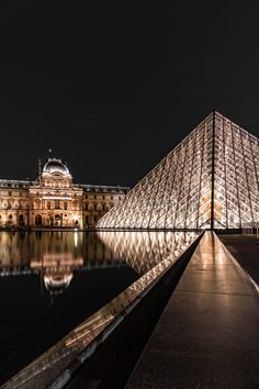 the pyramid is lit up at night in front of a building with its reflection on the water