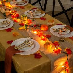 the table is set with plates, silverware and pumpkins on it for fall dinner