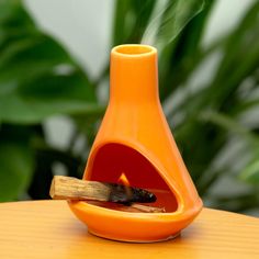 an orange vase sitting on top of a wooden table next to a burning matchstick