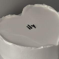 a white cake with icing and black writing on it's side, in the shape of a heart