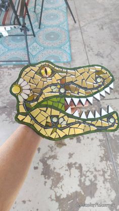 a hand is holding up a stained glass alligator's head with flowers on it