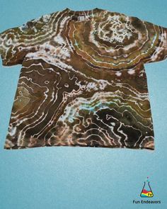 a t - shirt that is on top of a blue surface with white and brown swirls