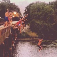 several people jumping into the water from a bridge over a body of water with a train in the background