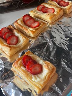 several pastries with strawberries on top of them sitting on aluminum foil lined up