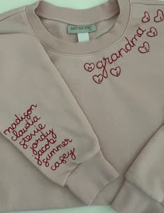 a pink sweater with red writing on the chest and two hearts embroidered on the sleeves