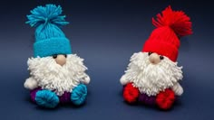 two knitted gnomes sitting next to each other on a blue surface with one wearing a red and white hat