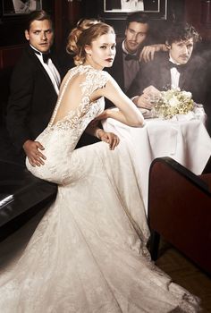 a woman in a wedding dress sitting on a couch with two men standing behind her