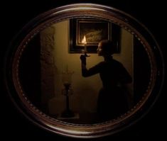 a woman holding a lit candle in her right hand and looking at it through a mirror