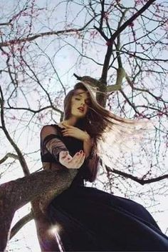 a woman standing on top of a tree with her hair blowing in the wind and looking up