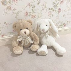 two stuffed animals sitting next to each other in front of a wallpapered wall