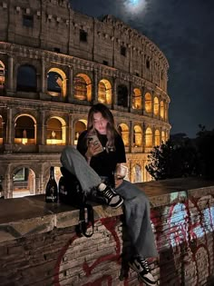 a woman sitting on top of a brick wall next to an old roman collise