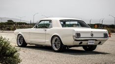 an old white mustang is parked on the side of the road