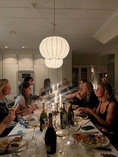 a group of people sitting around a dinner table with food and wine glasses on it