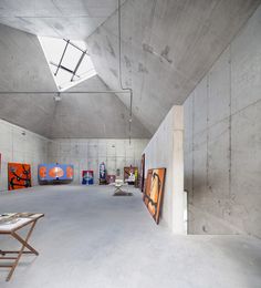 an empty room with paintings on the wall and a table in the middle, surrounded by concrete walls