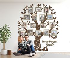 a man and woman sitting next to each other in front of a tree with family pictures on it