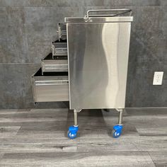 a stainless steel cabinet with five drawers and blue rollers on the bottom, in front of a gray wall