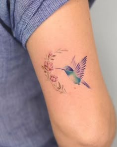 a small hummingbird tattoo on the right side of the left arm, with pink flowers around it