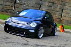 a black car parked in front of a stone wall with an orange flag hanging from it's side