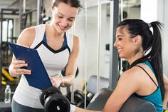 two women working out in a gym with dumbs on each side and one holding a clipboard